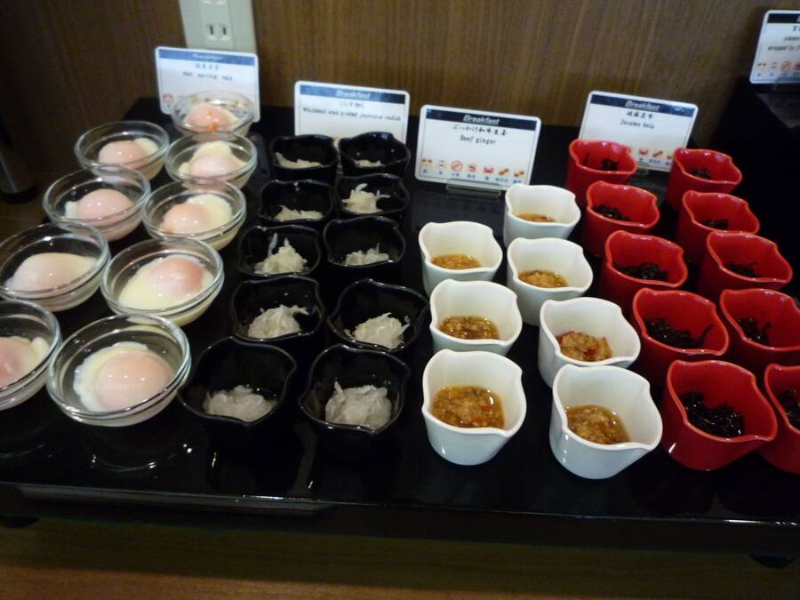 A variety of food items displayed in small bowls, each labeled with different names and prices.