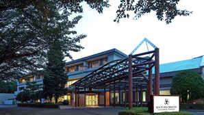 A modern hotel entrance with a covered walkway, a sign indicating the name 'Route Inn Grantia', and a parking area. - Route-Inn Grantia Fukuokamiyawaka-wakitaonsen- (Miyawaka)