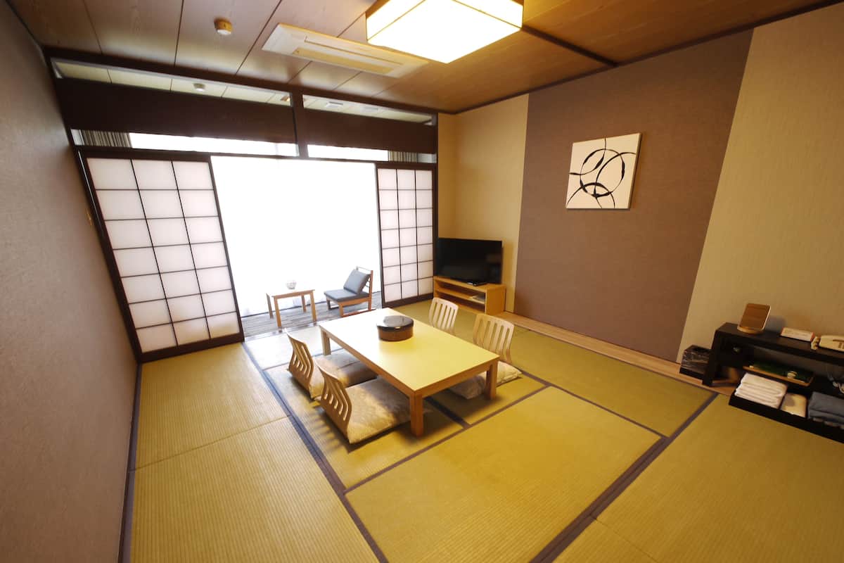 A traditional Japanese room with tatami flooring, a low table, chairs, a television, and a sliding door.
