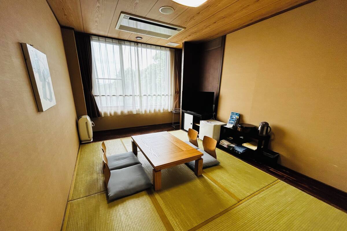 Perinteinen japanilainen huone, jossa on tatamimatto, matala pöytä, tyynyjä, televisio ja pieni kaappi.