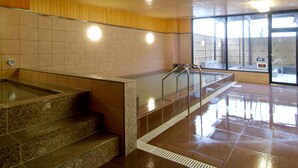 A public bath area with a stone bench, metal handrails, tiled walls, and a wooden panel accent. - Route-Inn Grantia Dazaifu (Dazaifu)
