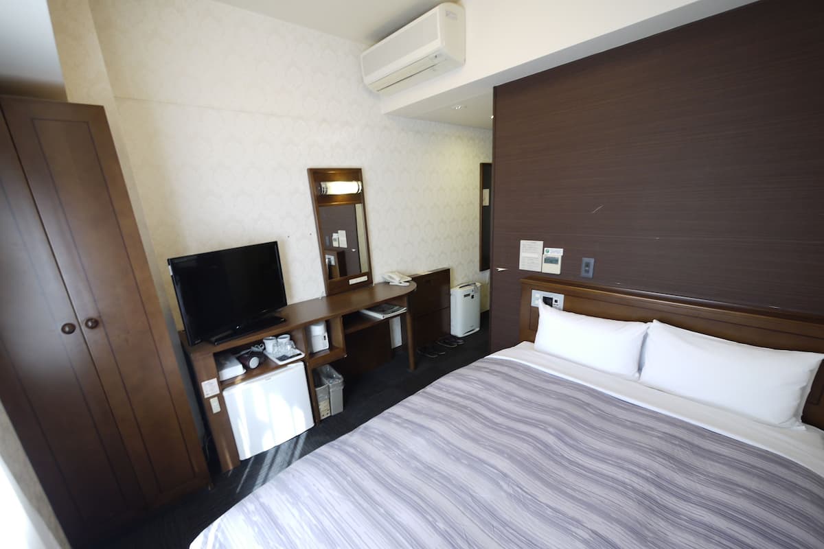 Une chambre d’hôtel comprenant un lit, un bureau avec une télévision, un miroir et une armoire.
