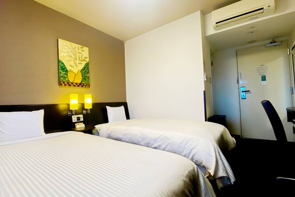 Ett hotellrum med två sängar, en väggmonterad luftkonditioneringsanläggning och en tavla ovanför sängarna.
