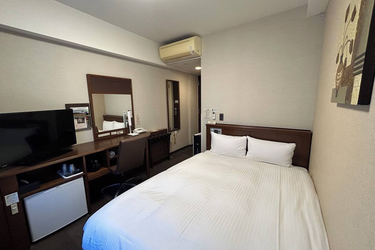 A hotel room with a bed, a desk with a computer, a television, and a mirror.