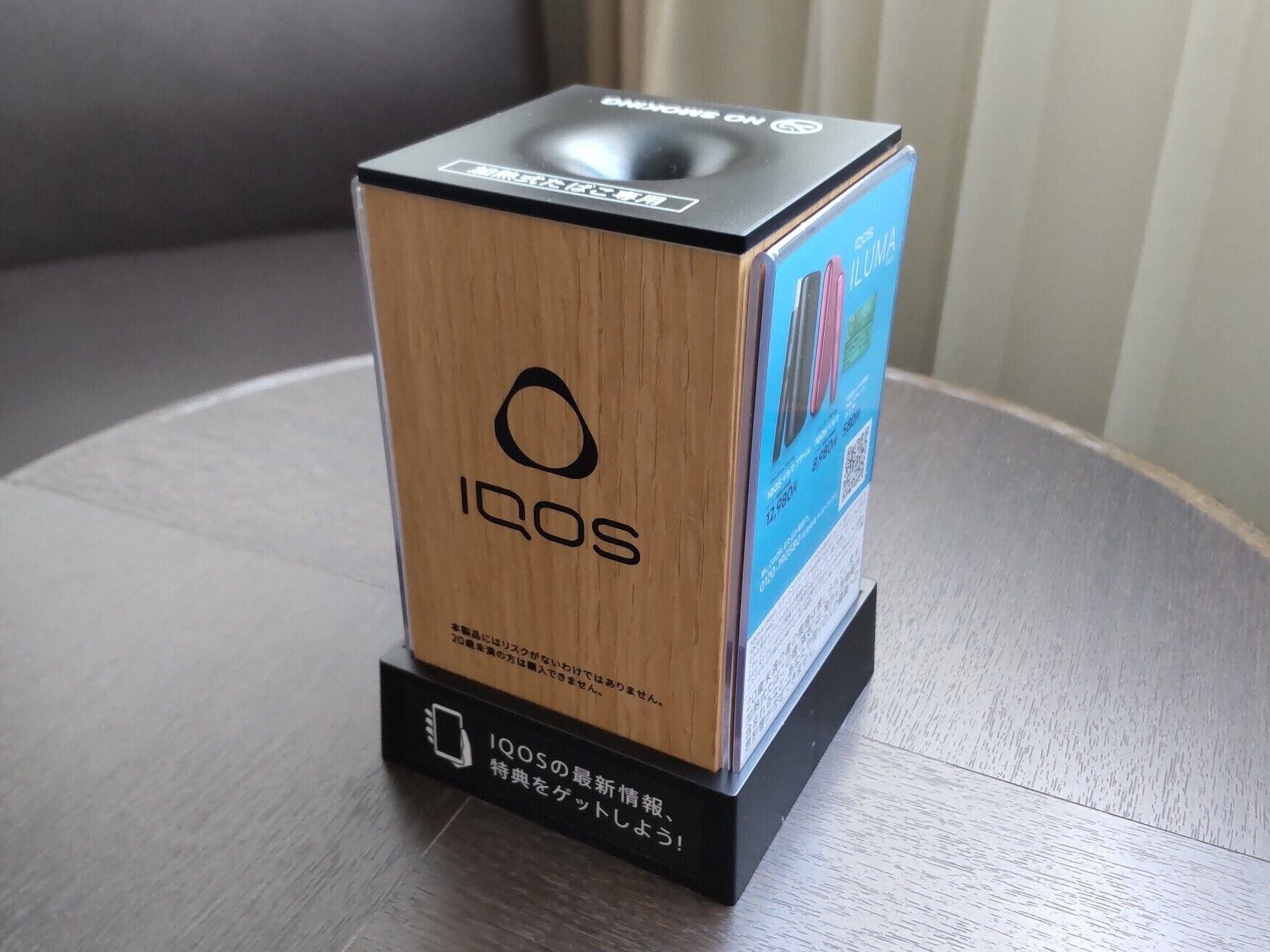 A wooden box with the Iqos logo and Japanese text, placed on a table.