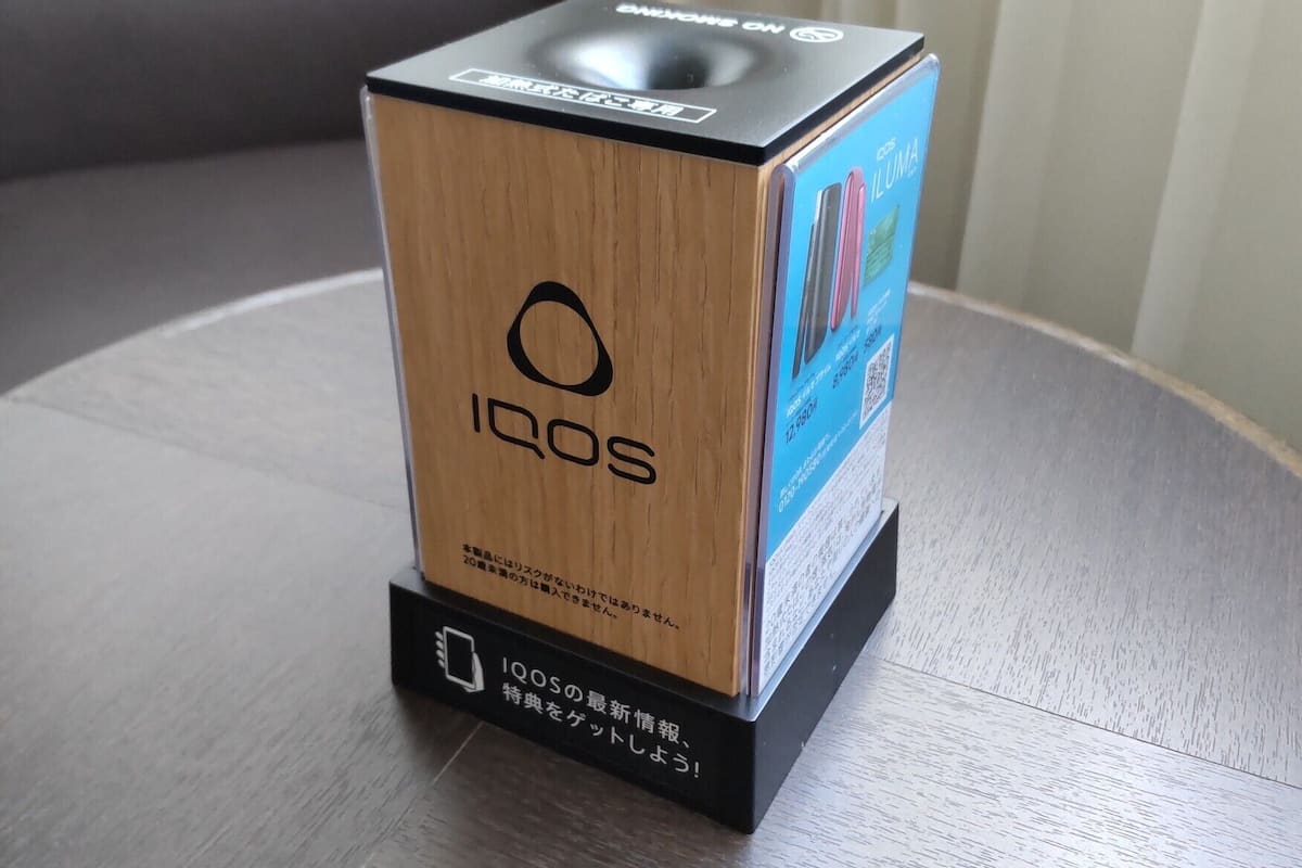 A wooden box with the Iqos logo and Japanese text, placed on a table.