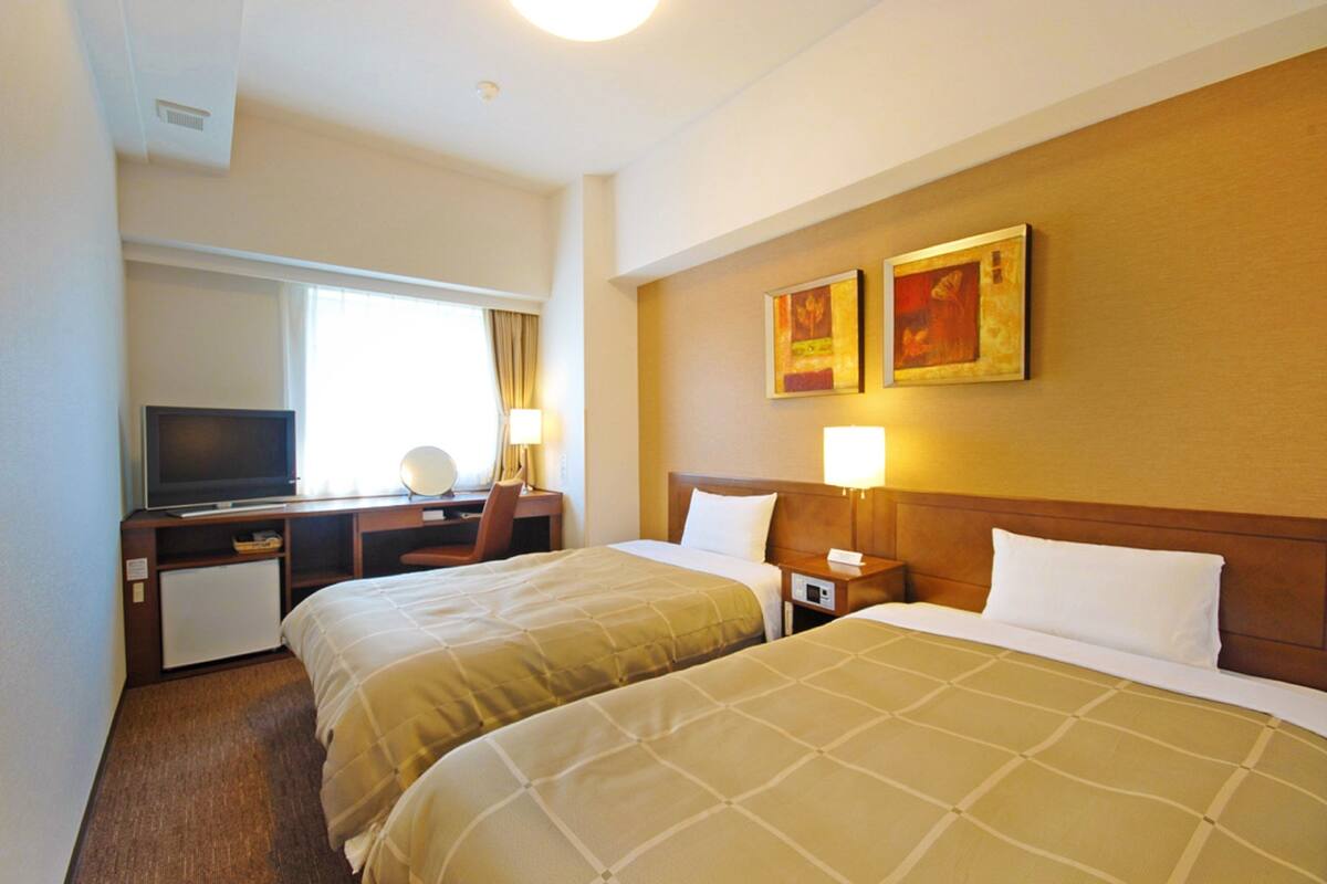A hotel room with two beds, a desk with a television, and artwork on the wall.