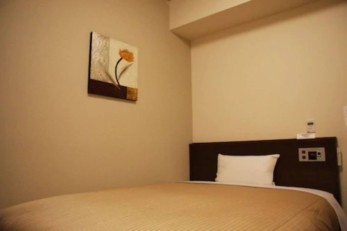 Quarto de hotel com cama, painel de controle e um quadro na parede.