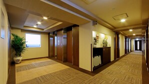 Ein Hotelkorridor mit Teppichböden, Holztüren und einem Empfangsbereich mit Pflanze.