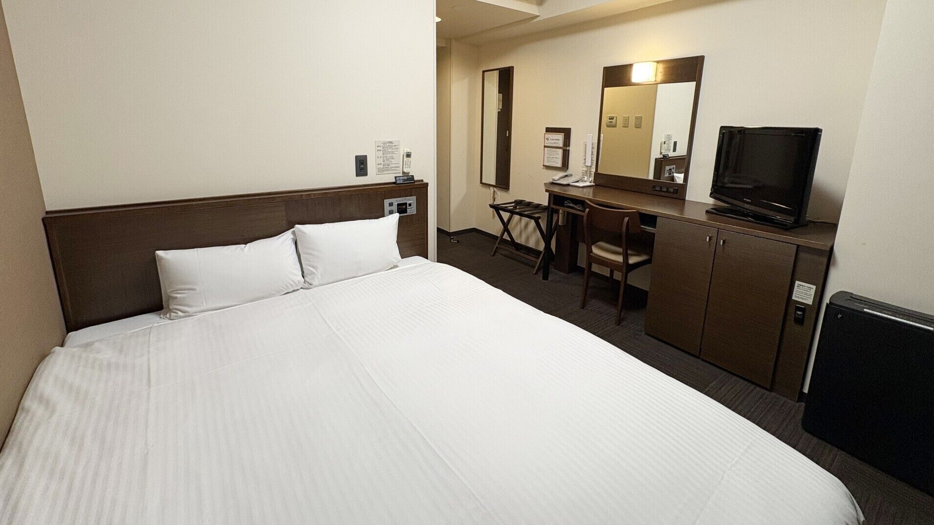 A hotel room with a large bed, a desk with a chair, a television, and a mirror.