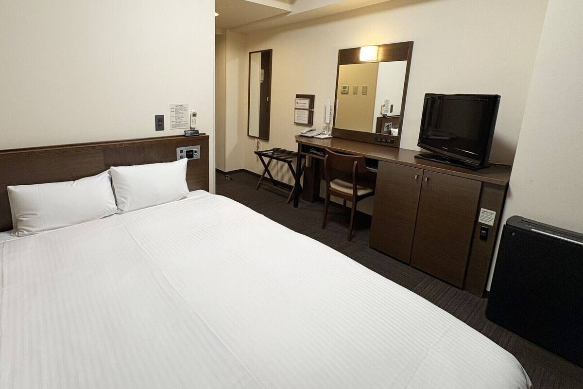 Une chambre d’hôtel avec un grand lit, un bureau avec une chaise, une télévision et un miroir.