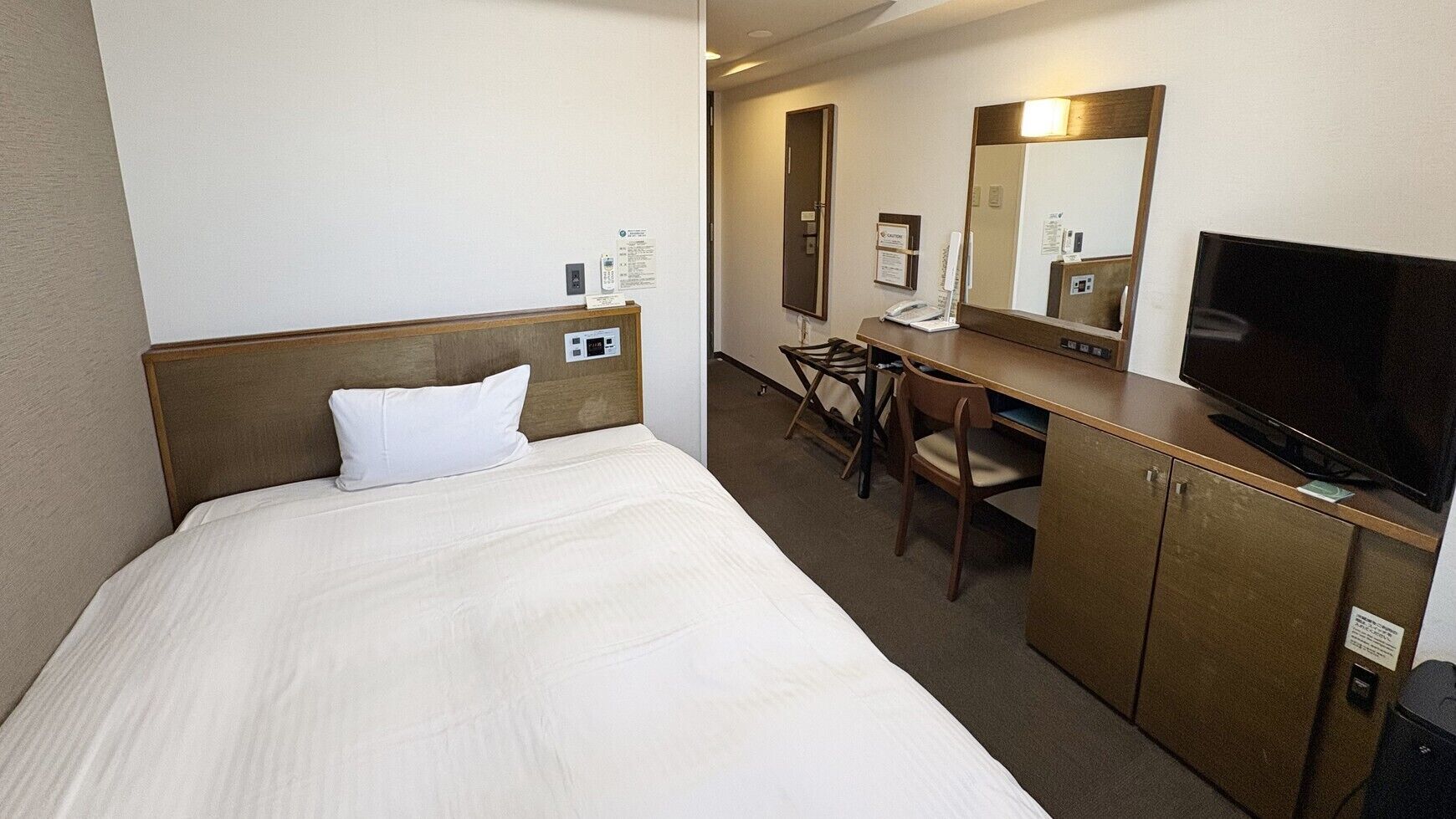 A hotel room with a bed, desk, chair, television, and a mirror.