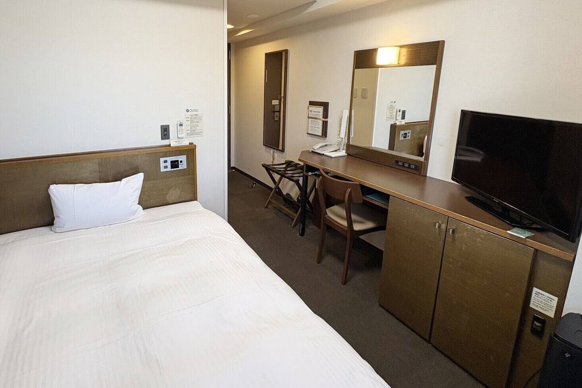 Une chambre d’hôtel équipée d’un lit, d’un bureau, d’une chaise, d’une télévision et d’un miroir.