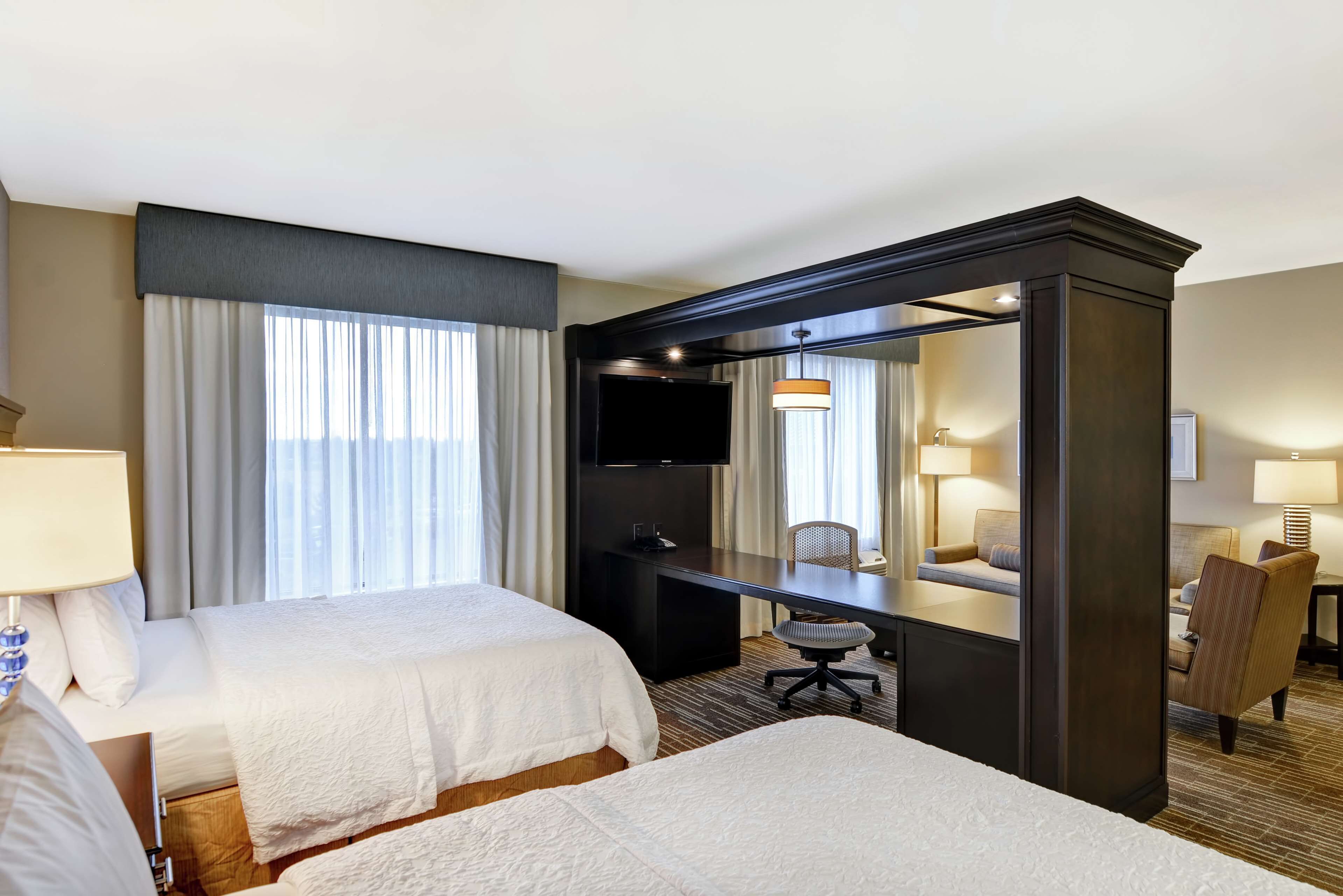 A hotel room with two beds, a desk, a chair, a TV, and a large mirror.