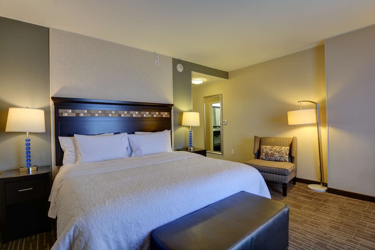 A hotel room with a large bed, two bedside tables with lamps, a chair, and a small table.