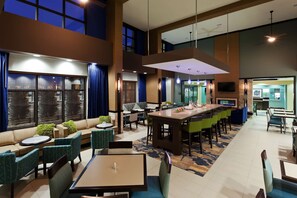A modern hotel lobby with a dining area, sofas, and a bar. - Hampton Inn & Suites- Denver/Airport-Gateway Park (Denver)