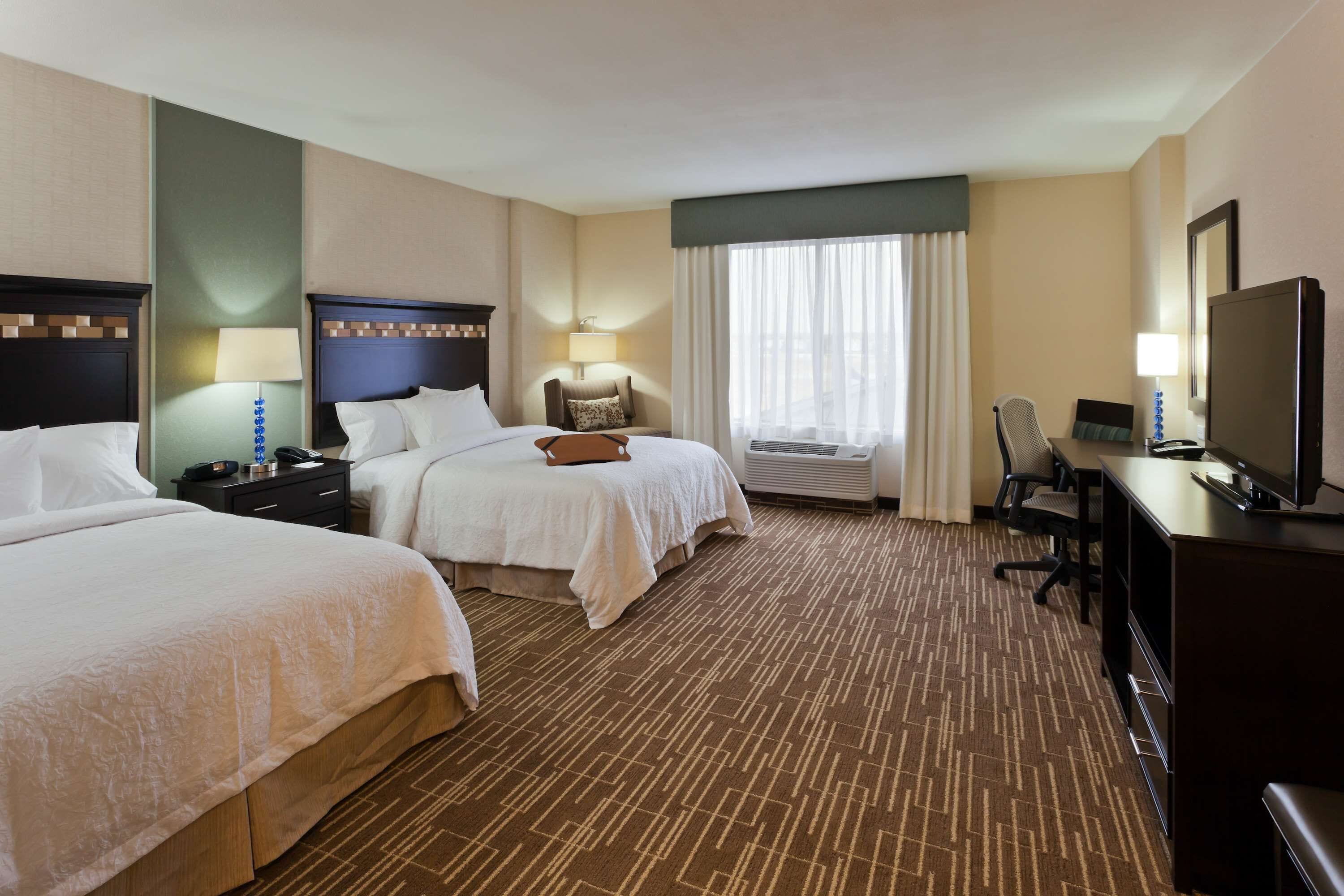 A hotel room with two beds, a desk, a television, and a window with curtains.