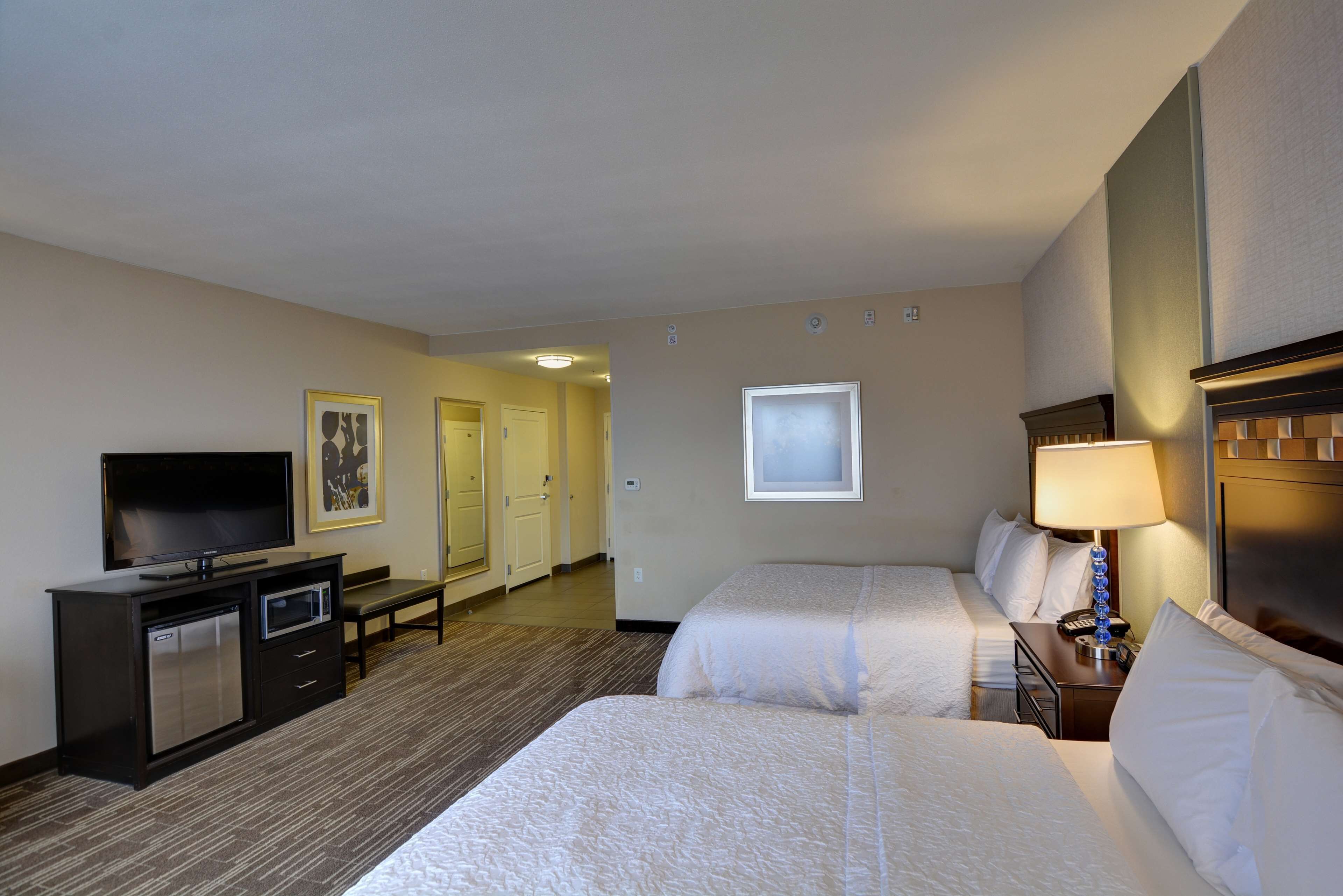 A hotel room with two beds, a TV, a desk, and a lamp.