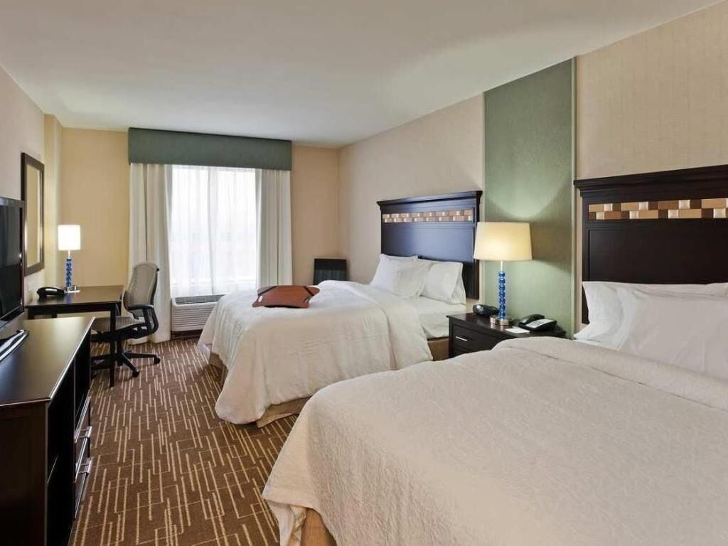 Habitación de hotel con dos camas, un escritorio, una silla, un televisor y una ventana con cortinas.