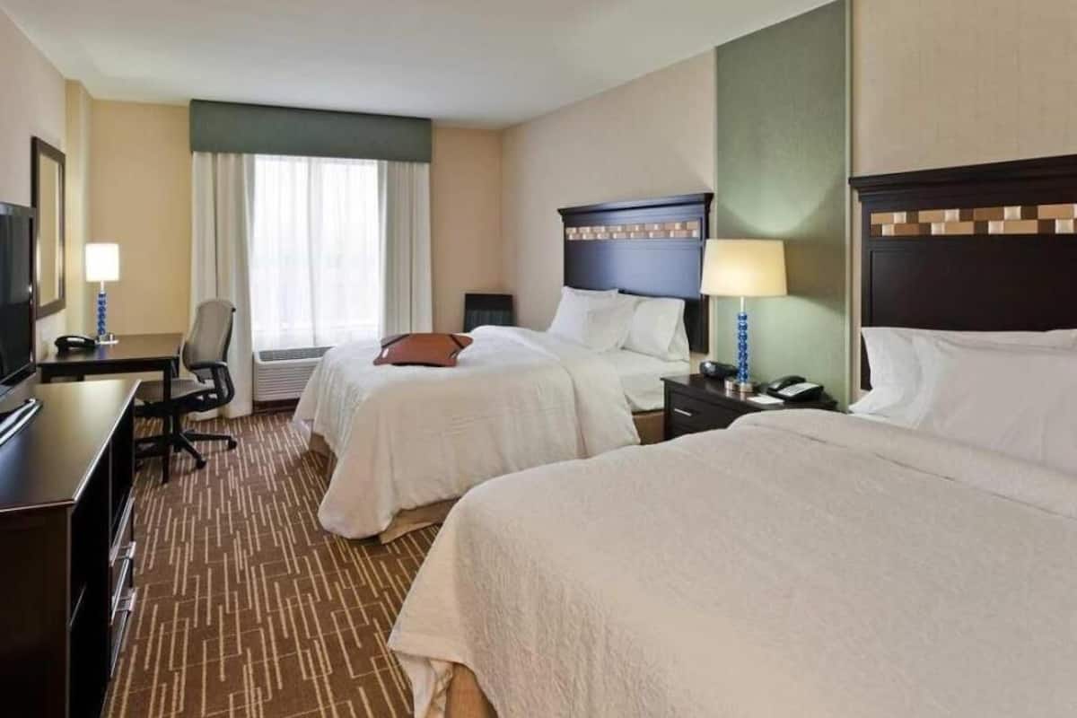 Habitación de hotel con dos camas, un escritorio, una silla, un televisor y una ventana con cortinas.