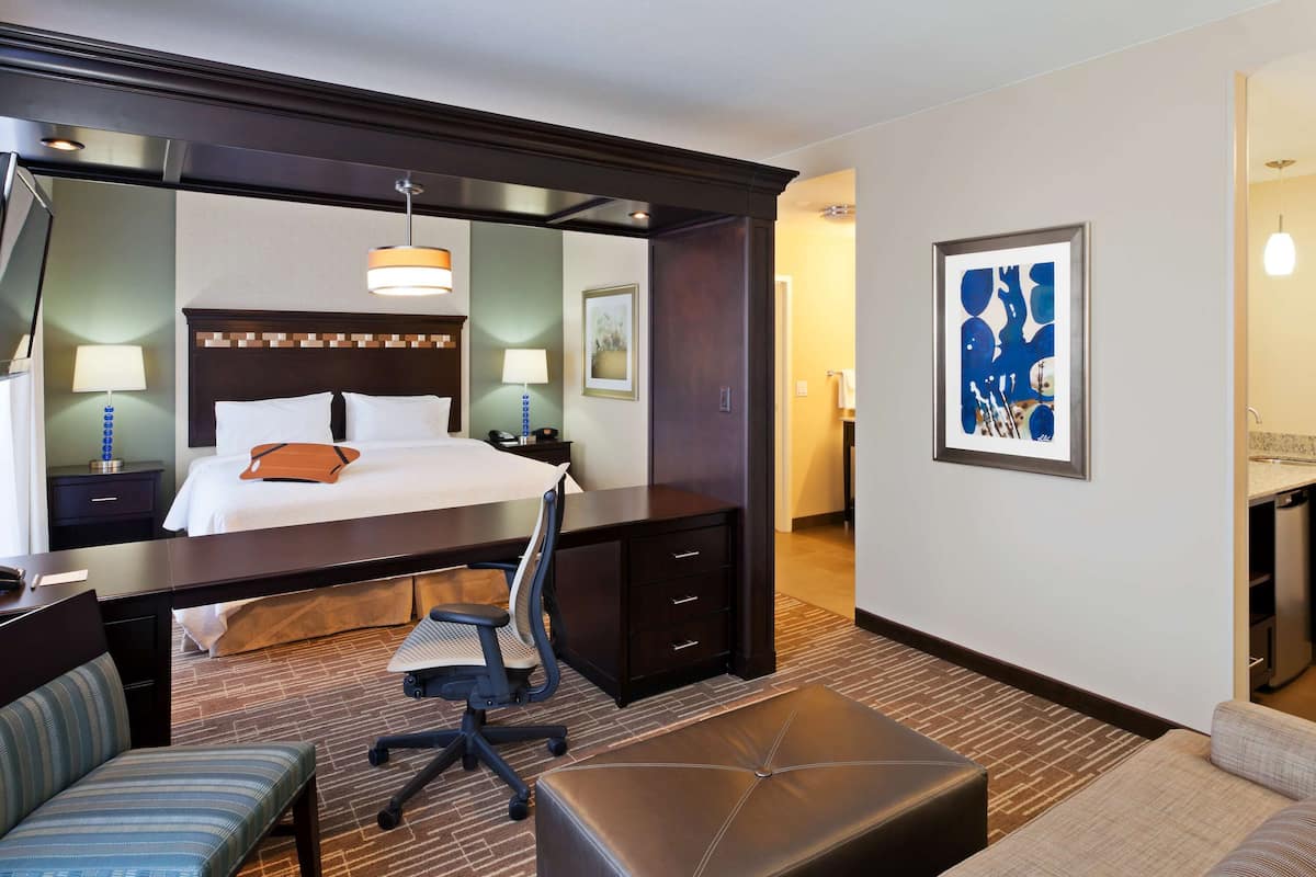 A hotel room with a large bed, a desk, a chair, a sofa, and a small table.