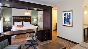 A hotel room with a large bed, a desk, a chair, a sofa, and a small table.