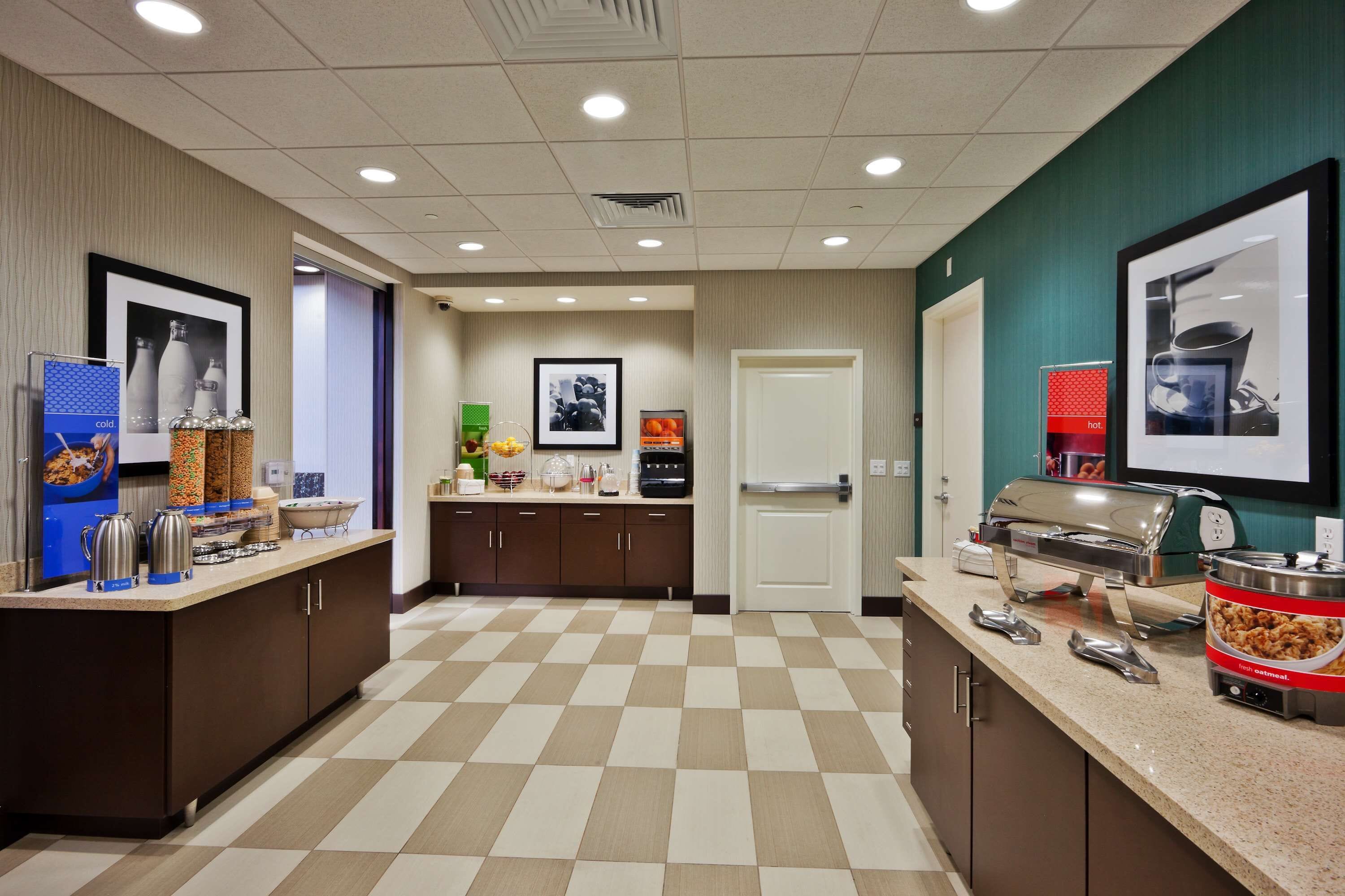 Una cocina de hotel con piso a cuadros, un mostrador de buffet con recipientes de comida y un refrigerador.