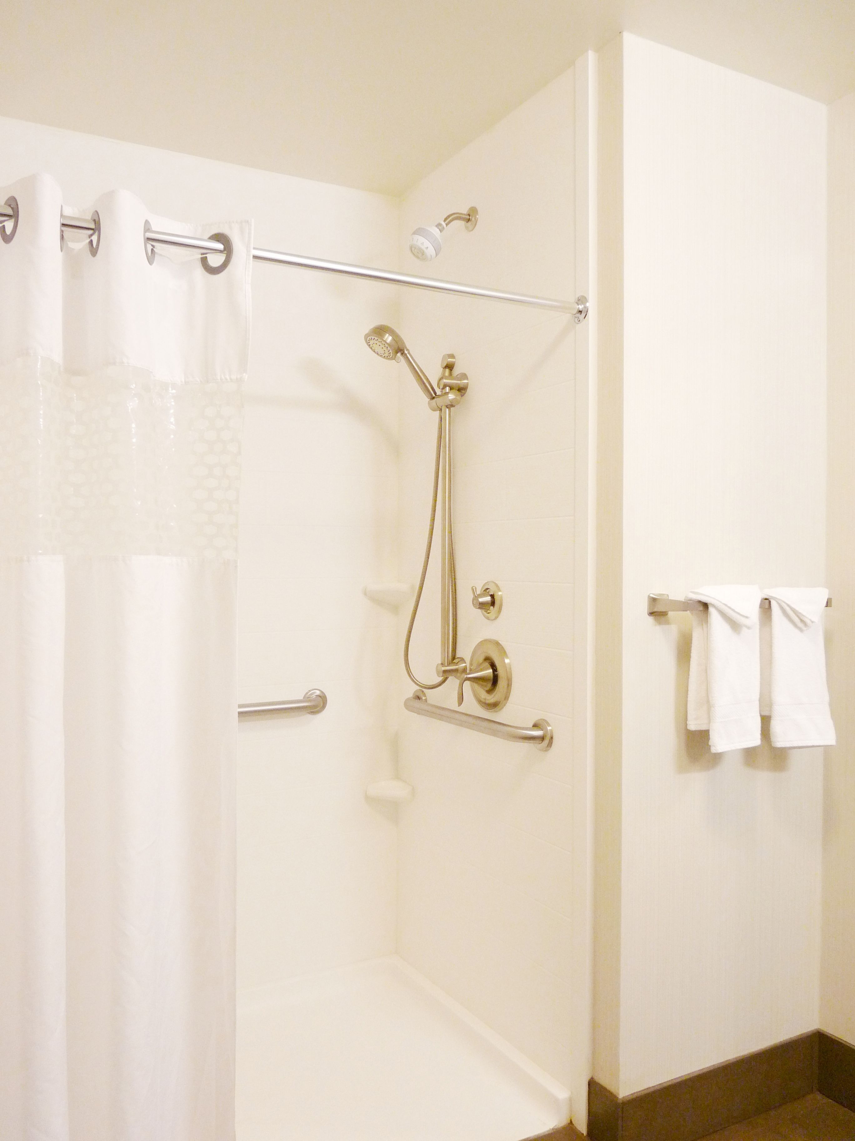 A shower area with a handheld showerhead, grab bars, and a towel rack with towels.
