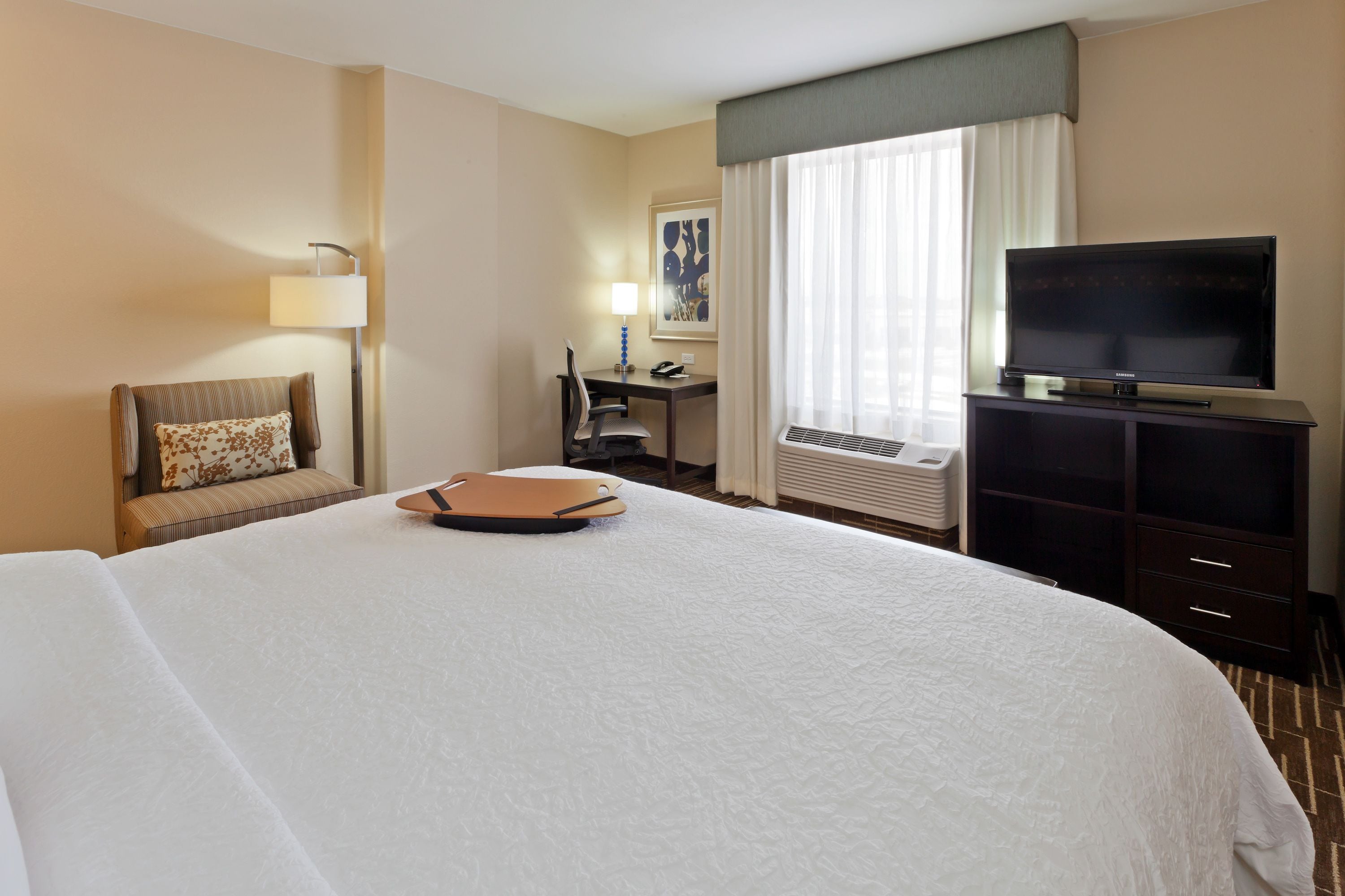 A hotel room with a large bed, a desk with a chair, a television, and a lamp.