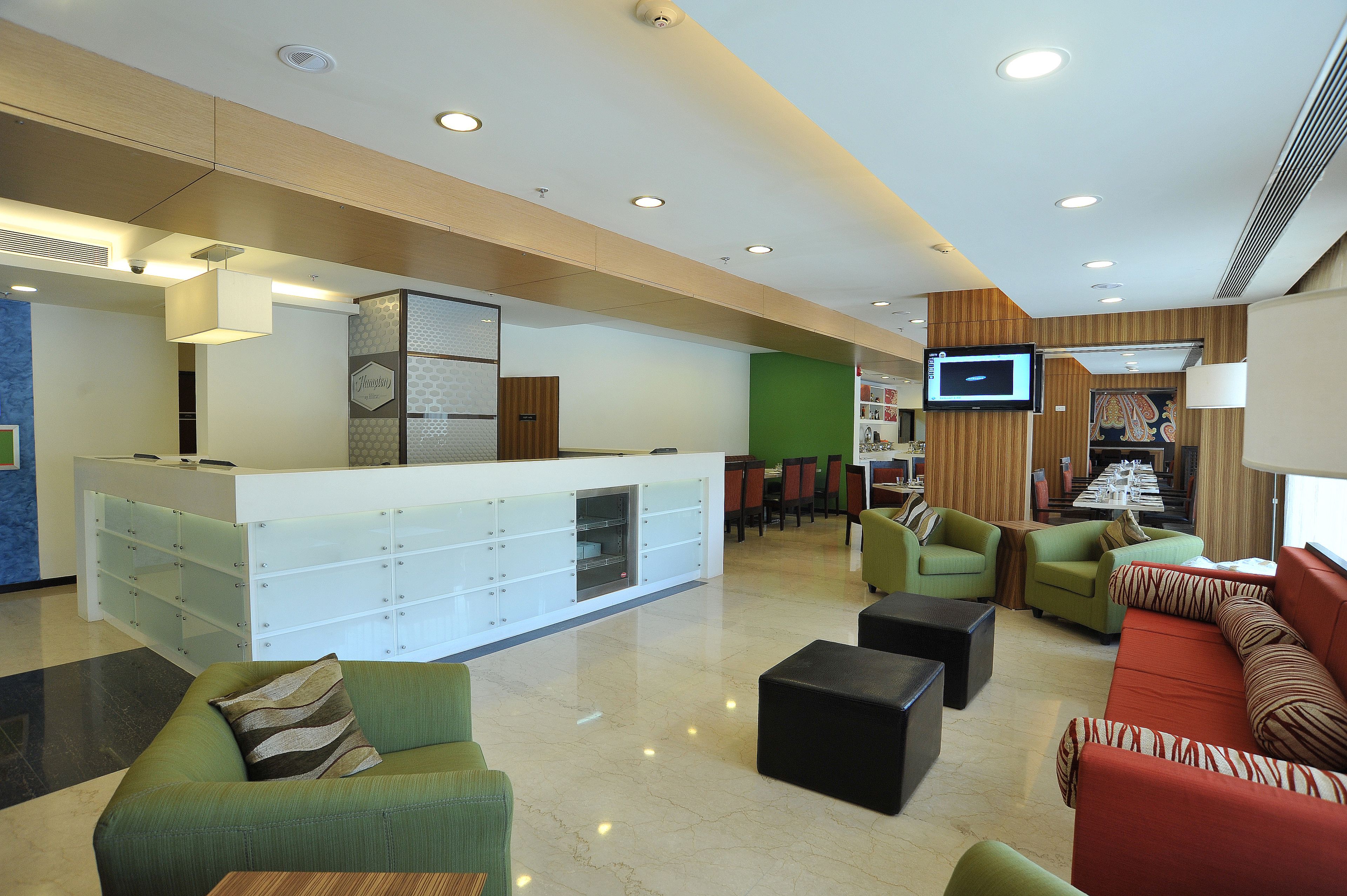 A modern lobby with a reception desk, seating area, and a TV screen.