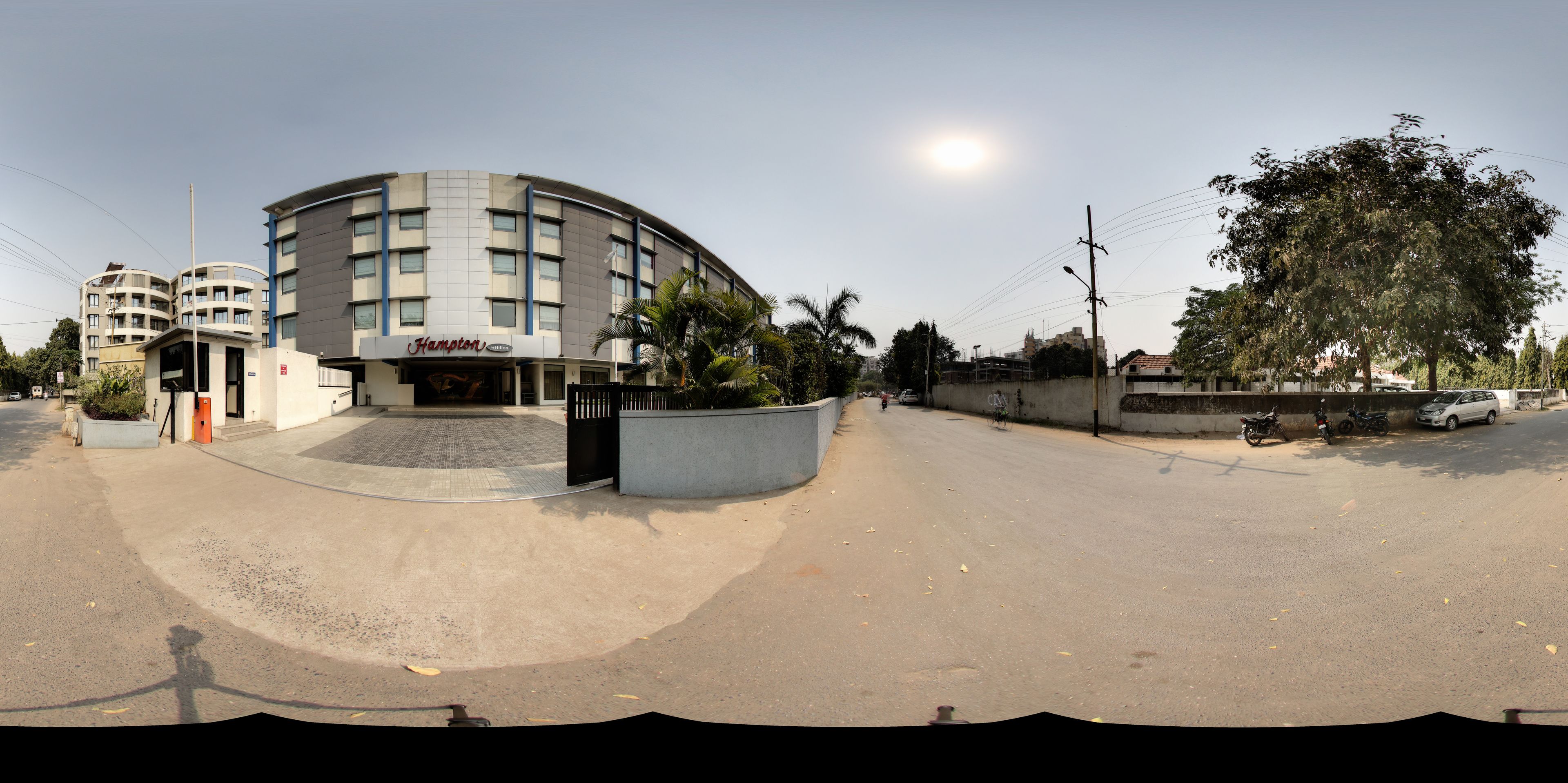 A curved hotel building with a 'Hampton' sign, a gated entrance, and a paved driveway.