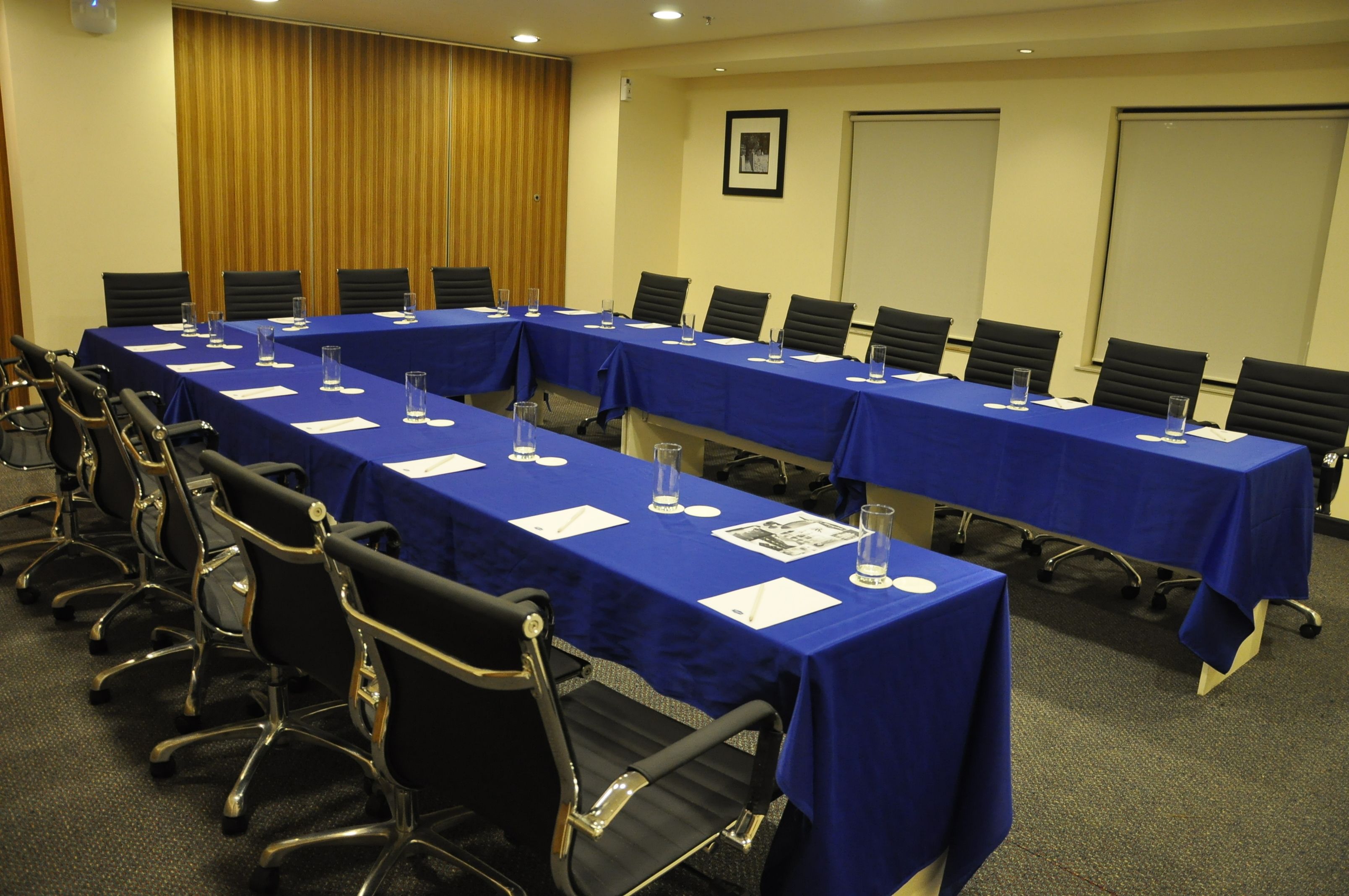 A conference room with long tables covered in blue tablecloths, equipped with chairs and water glasses.