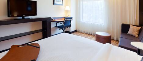 Una habitación de hotel con cama, escritorio y silla, televisor, ventana con cortinas y sofá.