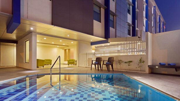 Una piscina con azulejos de mosaico azul, una zona de estar con sillas y un edificio con balcón.