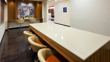 A modern bar area with a long counter, three cushioned bar stools, and a large wall-mounted artwork.