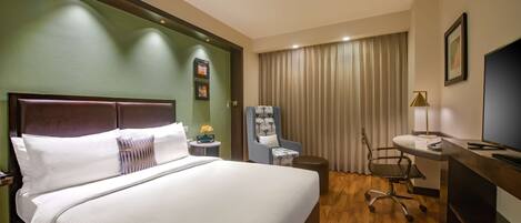 Habitación de hotel con una cama grande, un escritorio con silla, un televisor y una ventana con cortinas.