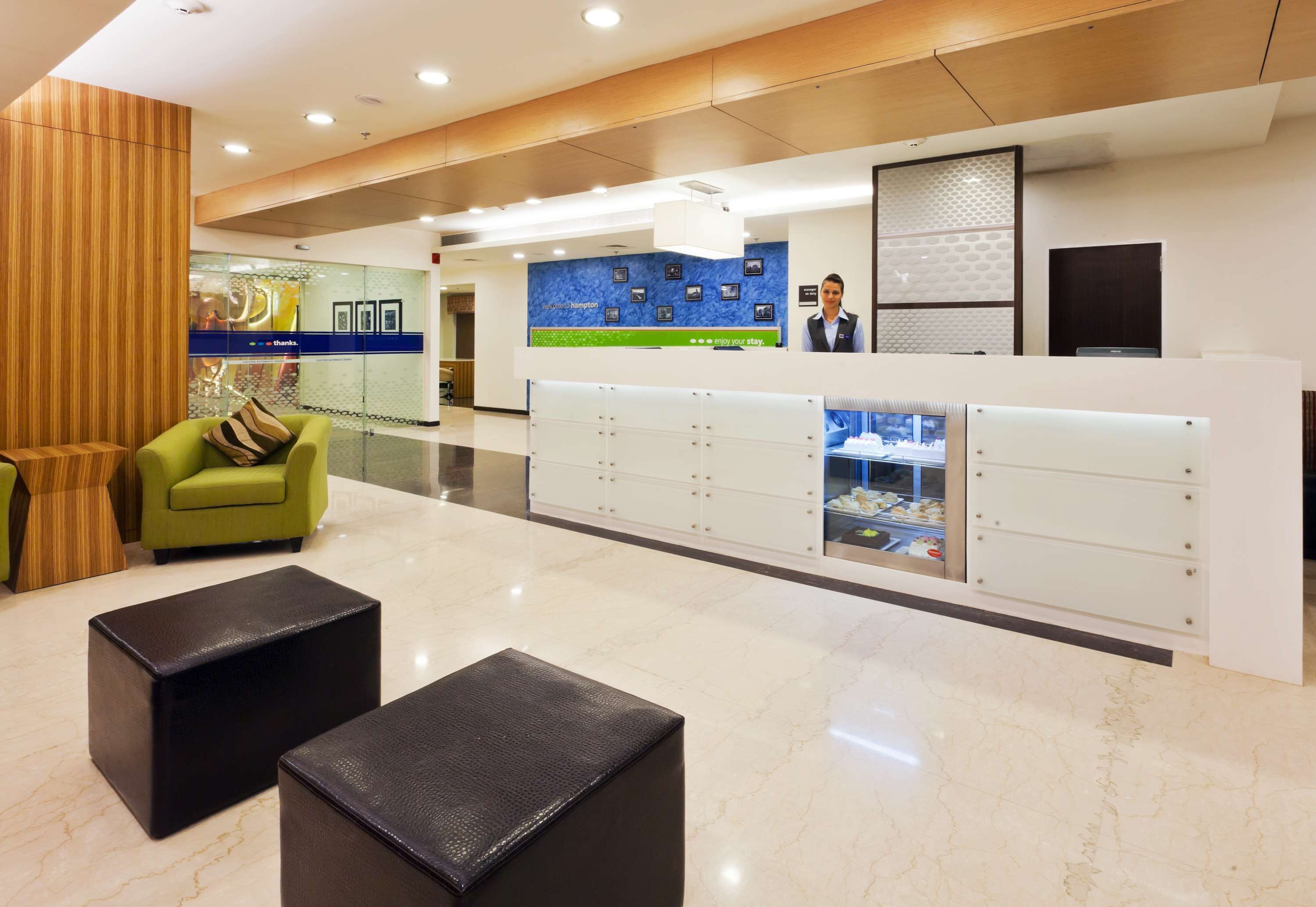 A modern hotel lobby with a reception desk, seating area, and a glass wall displaying a cityscape.