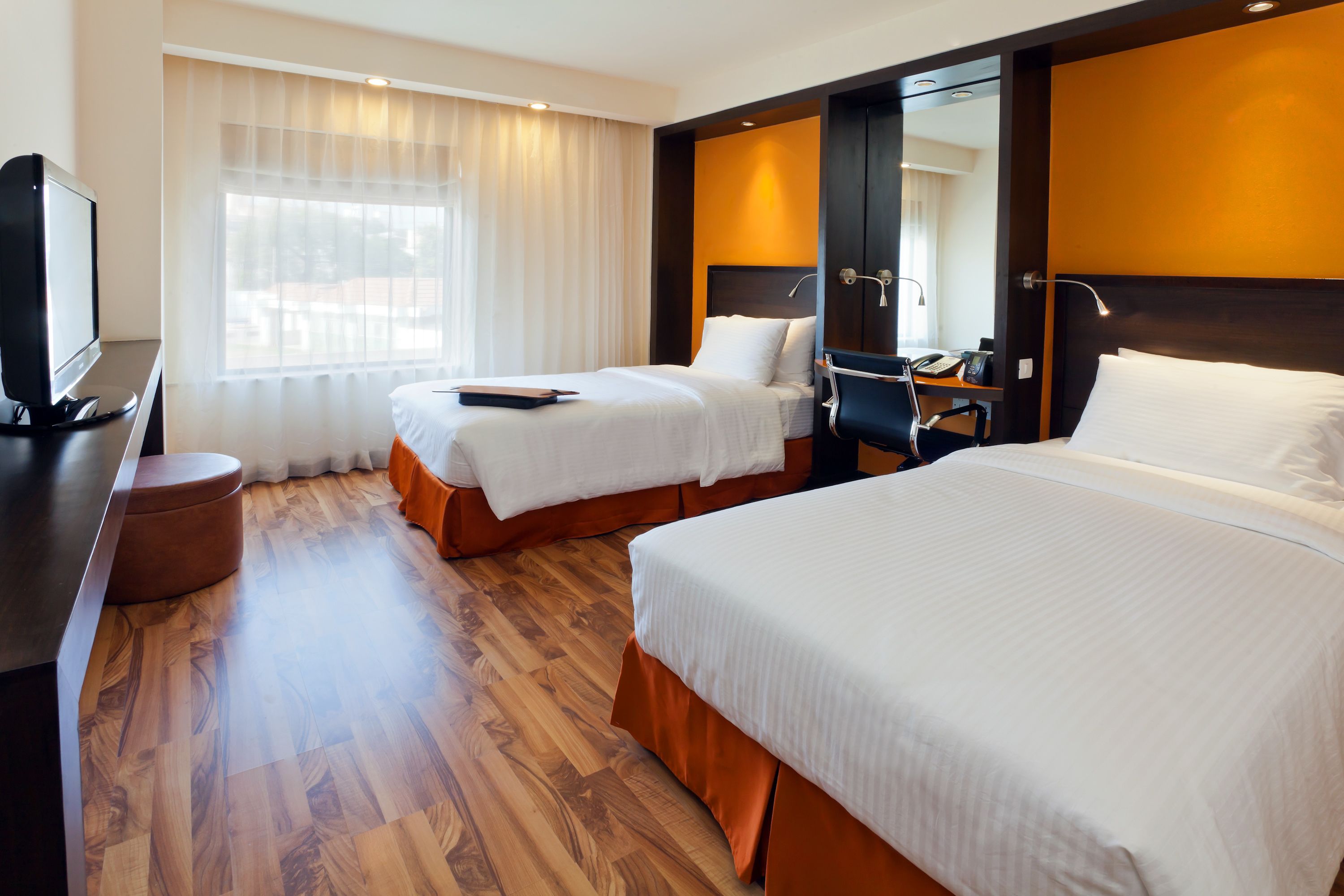 Habitación de hotel con dos camas, un escritorio, un televisor y una ventana con cortinas.