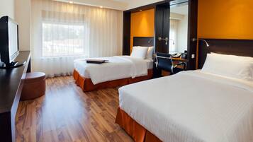Habitación de hotel con dos camas, un escritorio, un televisor y una ventana con cortinas.