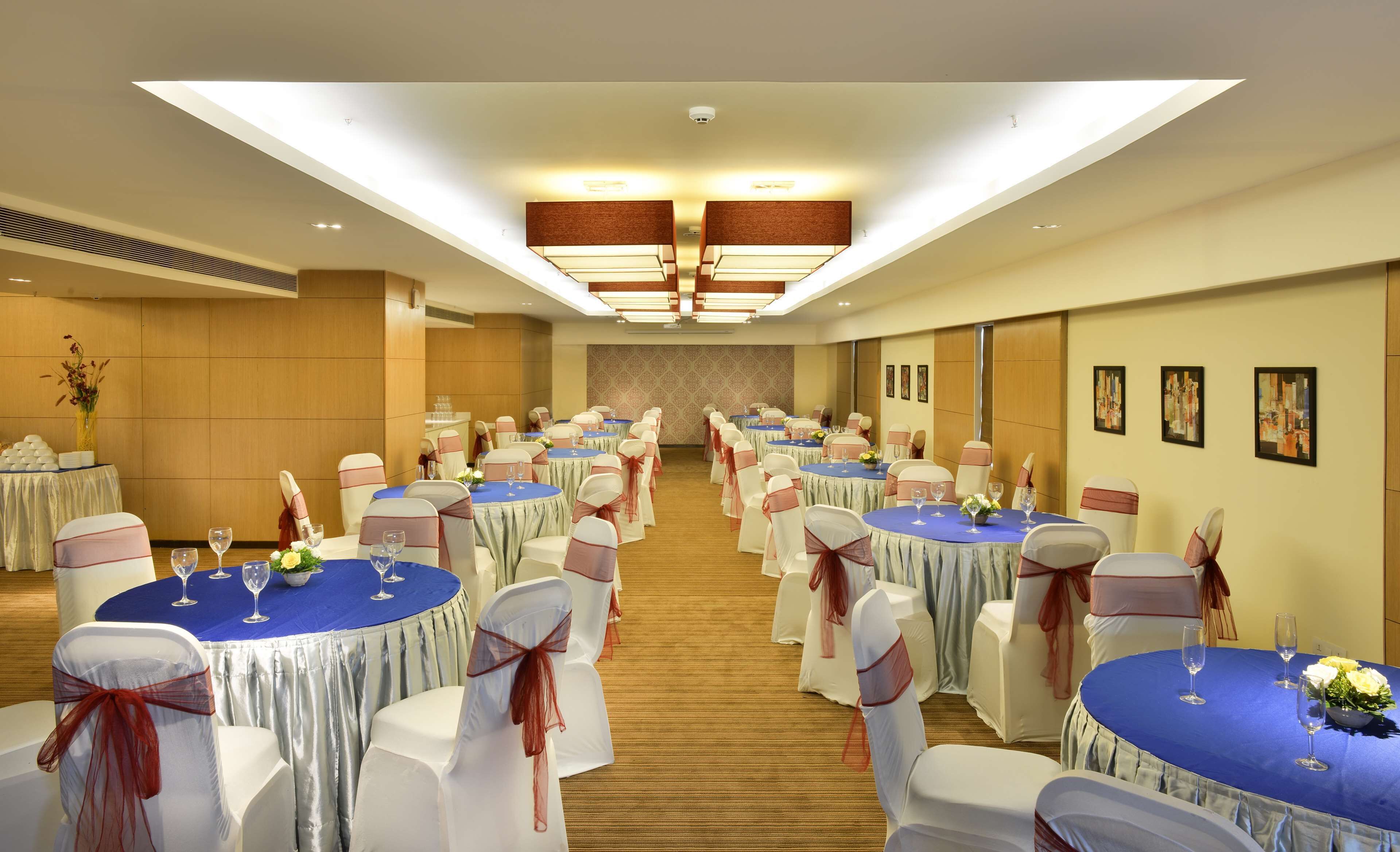 Un salón de banquetes con mesas redondas, sillas blancas y manteles azules.