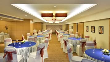 Un salón de banquetes con mesas redondas, sillas blancas y manteles azules.