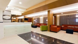 Un moderno vestíbulo de hotel con mostrador de recepción, zonas de estar y un gran ventanal con cortinas.