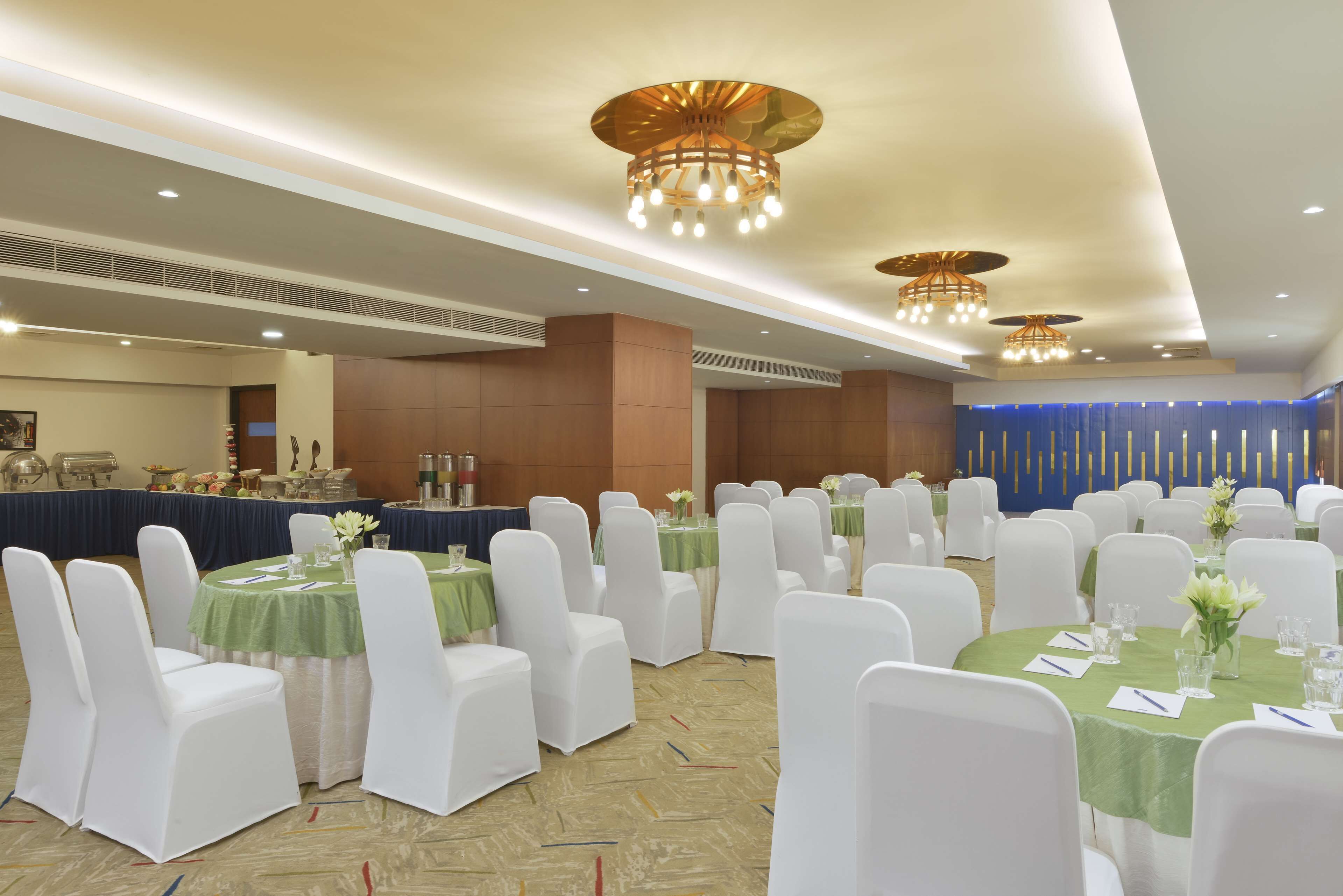Un salón de banquetes con mesas redondas, sillas blancas y manteles verdes.