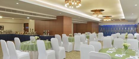 Un salón de banquetes con mesas redondas, sillas blancas y manteles verdes.