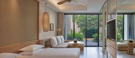 A modern hotel room with a large bed, a sofa, a TV, and a balcony with a view of greenery.