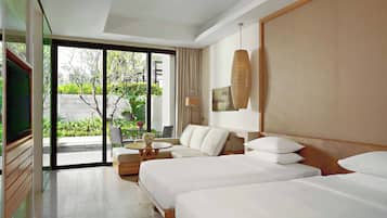 A hotel room with two beds, a sofa, a TV, and a balcony with a view of greenery.