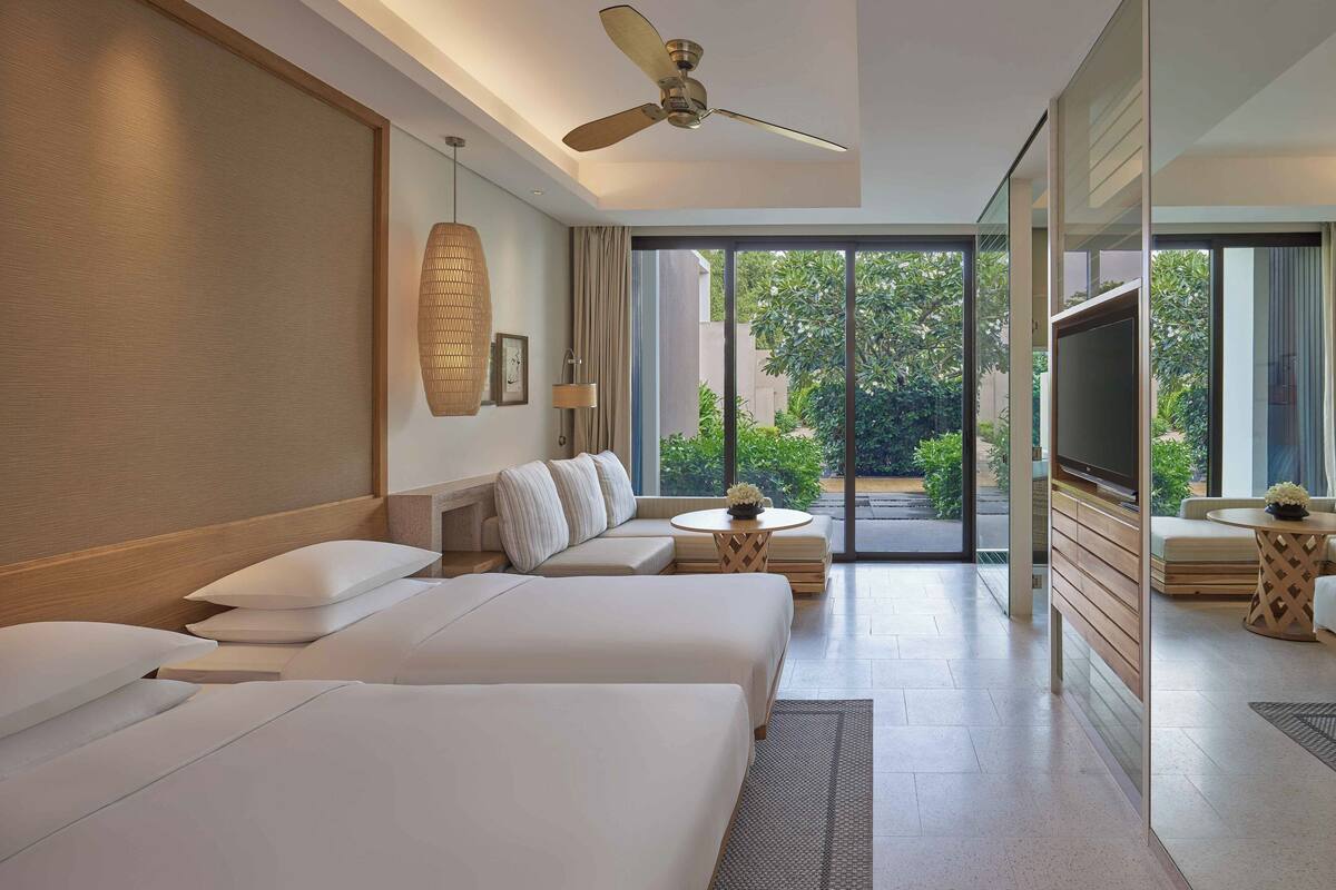 A modern hotel room with a large bed, a sofa, a TV, and a ceiling fan.