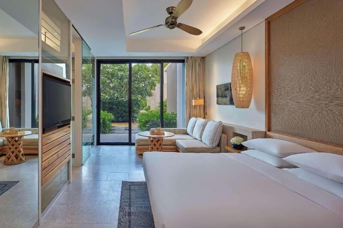 Una habitación de hotel moderna con una cama grande, televisión, ventilador de techo y vistas al exterior.