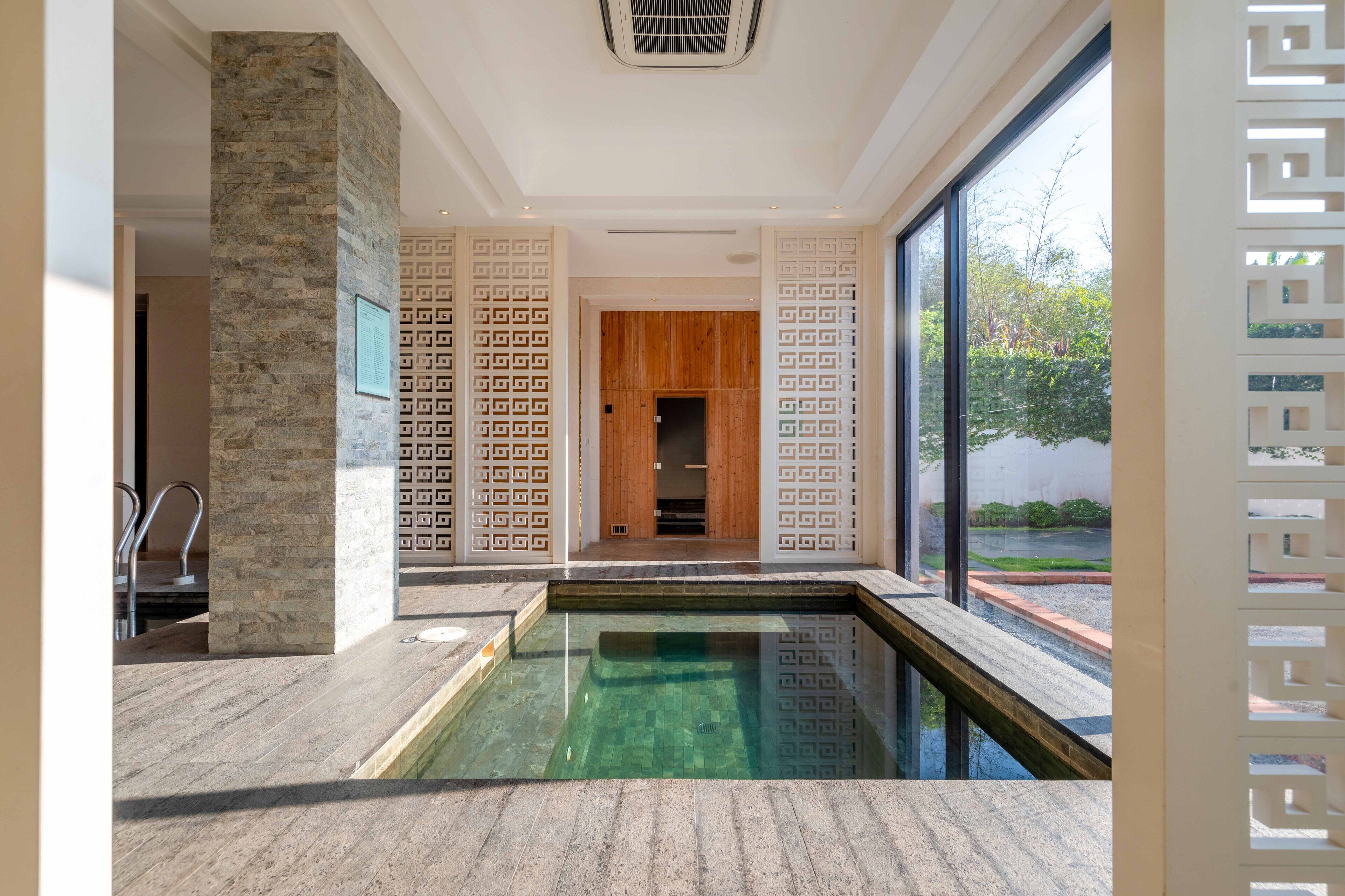 Une piscine intérieure moderne avec des murs en pierre et une porte en bois, de grandes fenêtres et une vue sur la verdure environnante.