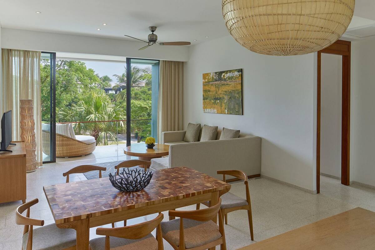 A modern living room with a dining area, large windows, and a ceiling fan.